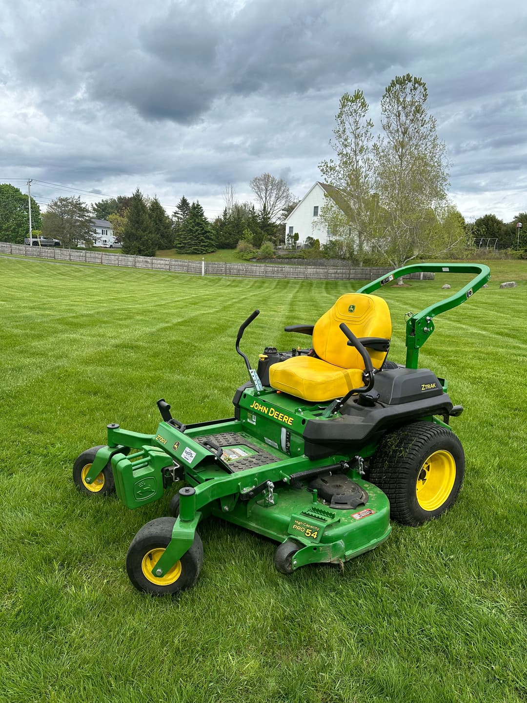 John Deere zero-turn lawn mower on a green lawn with cloudy skies in the background.