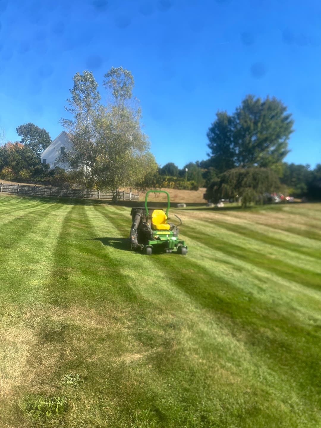 Lawn mower cutting grass in a green field under a clear blue sky.