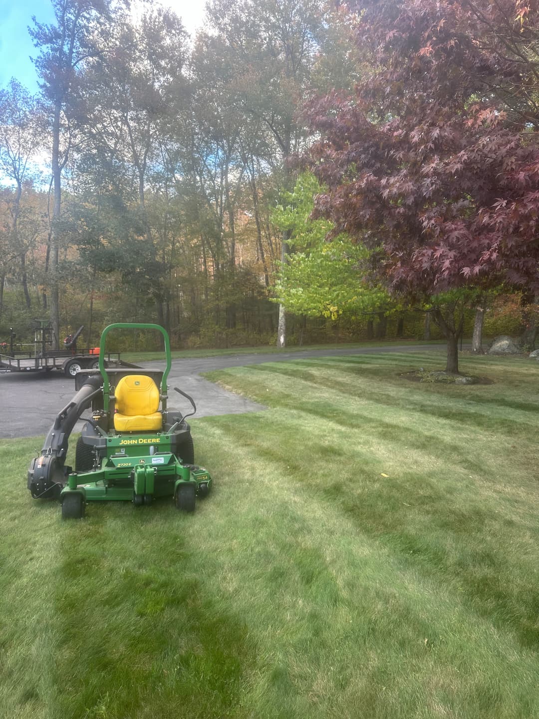 John Deere mower on freshly cut lawn with autumn trees in the background.
