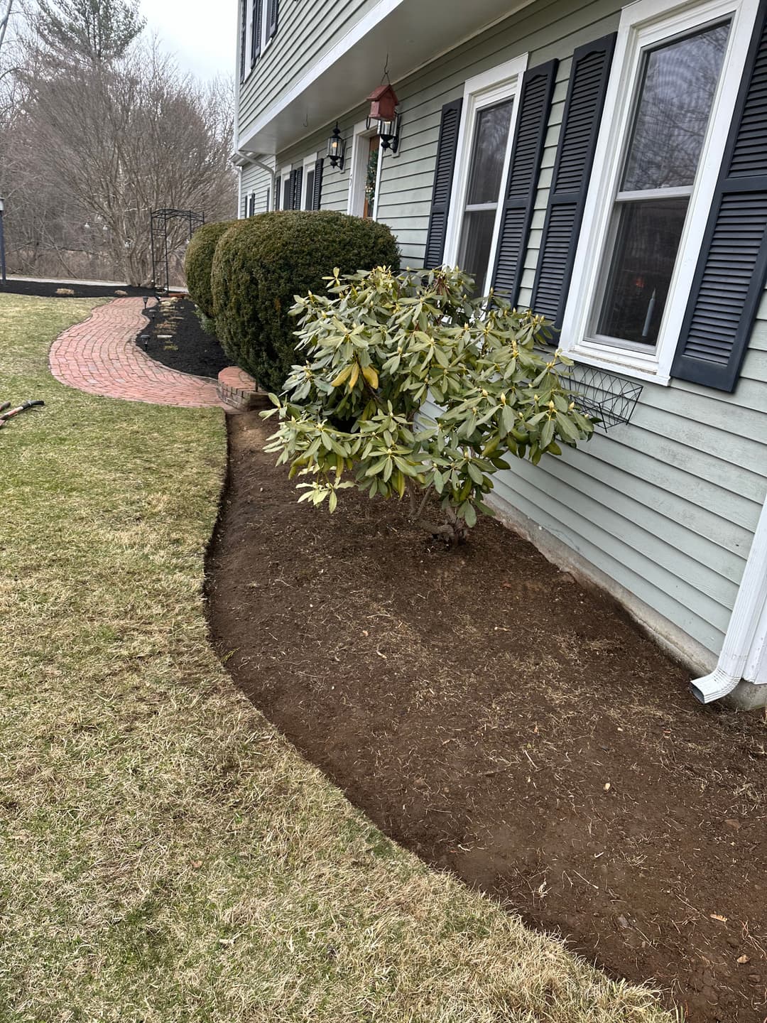 Landscaped yard featuring a curved flower bed, shrubbery, and a well-kept exterior of a house.