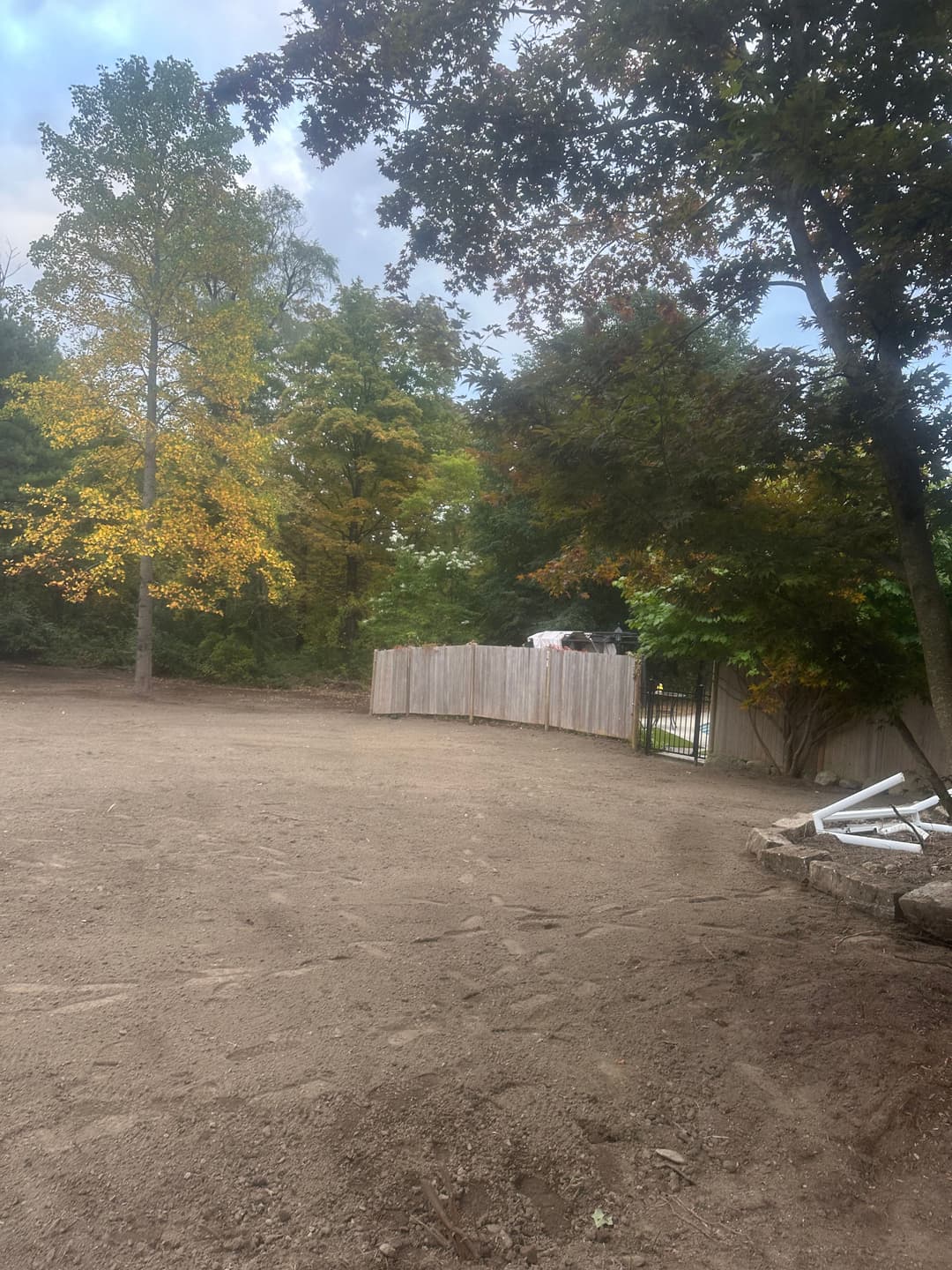 Cleared landscape with dirt ground, wooden fence, and autumn trees with yellow leaves.