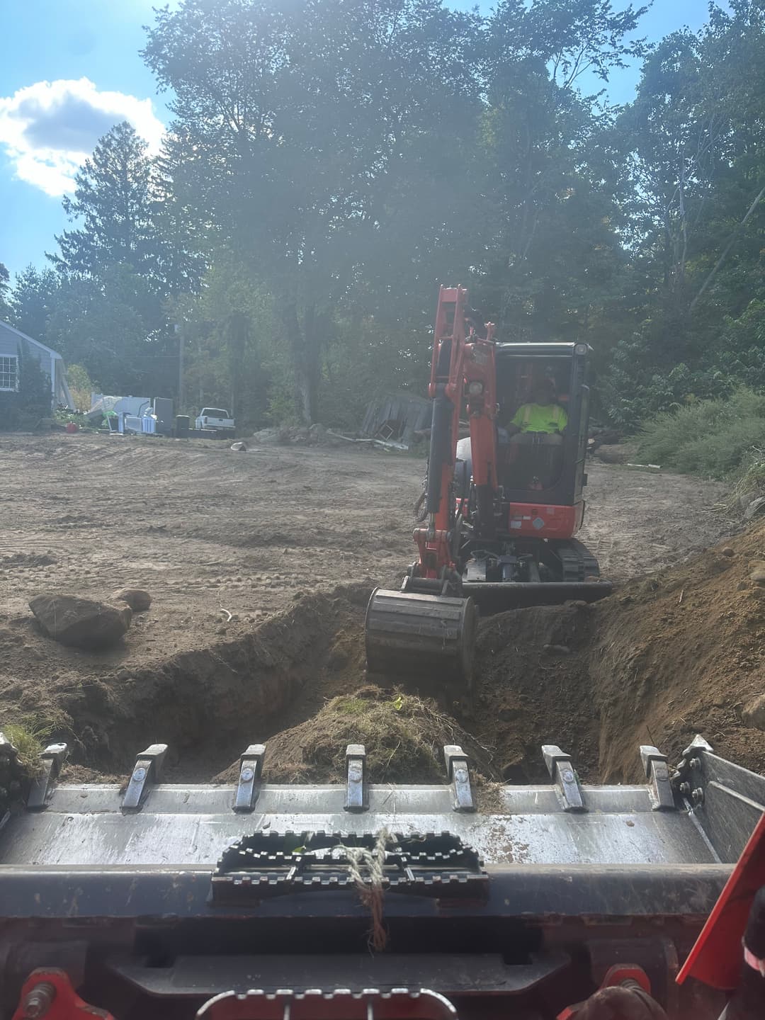 Excavator operating on cleared land, preparing for construction in a forested area.